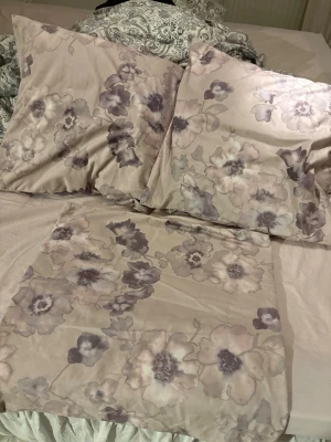 Beige blommiga kuddfodral / kuddar  - Säljer kuddar + fodral i beige med stora blommor i lila och grå toner. Knappt använda. 50x50