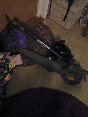 Svart elscooter Navee - Säljer en svart elscooter från Navee med robust ram och tydliga reflexer på framhjulet. Scootern har hopfällbar design och bred fotplatta, perfekt för smidig transport i stan. Laddas enkelt via eluttag och har tydliga handtag för bra grepp.