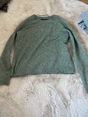Grön stickad tröja från Vero Moda - Mysig grönmelerad stickad tröja från Vero Moda med rund halsringning och långa ärmar. Tröjan har ribbstickade muddar vid ärmslut och nederkant, perfekt för lager-på-lager-stil. nypris ca 300-400, knappt använd! super vacker o säljer pga att jag inte använder den🥹 sänker pris vid snabbt köp!