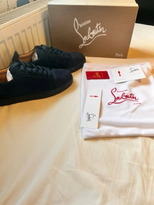 Christian Louboutin mörk blå sneakers - Snygga mörk blå sneakers från Christian Louboutin i mocka med klassisk röd sula och diskret broderad logga på sidan. Lågt skaft och mörk blåa skosnören ger en clean och exklusiv look. Perfekta för dig som vill sticka ut med stil. Pris ej hugget i sten!!!