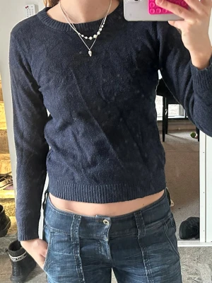 Mörkblå stickad tröja från Vila - Mörkblå stickad tröja från Vila med rund halsringning och långa ärmar. Tröjan har ribbade muddar vid ärmslut och nederkant, och är i en mjuk, lite tunnare stickning. Enkel och stilren modell som passar till mycket.