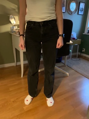 Svarta raka jeans med hög midja - Säljer ett par svarta jeans med rak passform och hög midja. Jeansen har klassiska fem fickor och stängs med knapp och dragkedja. Perfekta för dig som gillar en enkel och stilren look.