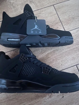 Svarta Air Jordan 4 Retro sneakers - Säljer ett par helsvarta Air Jordan 4 Retro sneakers med meshpaneler, synlig Air-sula och klassisk Jumpman-logga på plösen. Skorna har en robust siluett, svarta skosnören och detaljer i plast och mocka. Perfekta för dig som gillar streetwear och ikoniska modeller.
