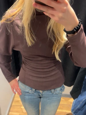 Brun långärmad topp med puffärm - Snygg brun långärmad topp med puffiga axlar och figurnära passform. Perfekt att styla med jeans eller kjol för en trendig look. Mjuk och skön känsla, passar dig som gillar stilrena basplagg med en twist.