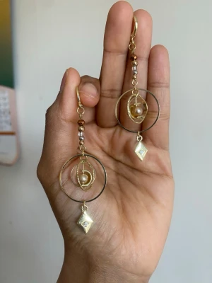 Guldiga statementörhängen med pärlor - Unika örhängen i guldton med flera cirklar, pärldetaljer och geometriska hängen. De har små och stora guldfärgade kulor längs kedjan och en vit pärla i mitten av cirklarna. Perfekta för dig som gillar att sticka ut med accessoarer.
