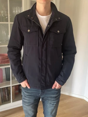 Mörkblå Fieldjacka från Riley - S - Jag säljer den här riktigt snygga fieldjackan ifrån Riley i storlek 46 vilket motsvarar S. Den är knappt använd och är i väldigt fint skick. Nypris låg på ca 2000kr och jag säljer den här för 799kr. Tveka inte att höra av er!