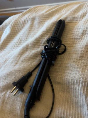 Svart plattång med sladd - En svart plattång med sladd och europeisk kontakt. Plattången har en smal och avlång form, tillverkad i plast och metall. Perfekt för att styla håret och skapa släta eller lockiga frisyrer. Enkel att använda och passar de flesta hårtyper.