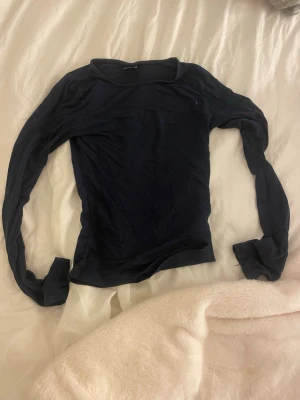 Mörkblå långärmad topp Gina Tricot - En enkel och stilren mörkblå långärmad topp från Gina Tricot. Modellen är tight och har en klassisk rund halsringning. Perfekt att matcha med jeans eller kjol för en clean look.