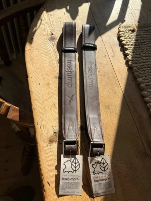 Freejump bruna stigläder läder - Säljer ett par bruna stigläder från Freejump i vegetabiliskt garvat läder. De har justerbara hål, svart kardborre och Freejump-logga tryckt på lädret. Perfekt till ridning och sadel, med robust och stilren design.