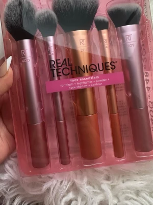 Real Techniques Face Essentials sminkborstar - Set med fem sminkborstar från Real Techniques i metallic rosa och koppar. Borstarna har mjuka, täta syntetiska borst och olika former för rouge, highlighter, puder, contour och nässkuggning. Perfekt för att skapa en jämn och snygg makeup.