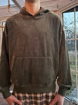 Hoodie - Säljer en mörkgrön hoodie i mjukt, sammetsliknande material. Hoodien har en stor magficka framtill, ribbade muddar vid ärmslut och nederkant samt en klassisk huva. Perfekt för en chill och avslappnad stil. Den har en fläck som går bort i tvätten, se sista bild.
