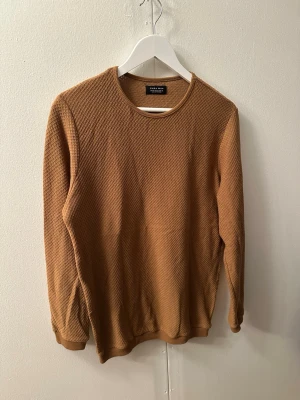 Brun stickad tröja från Zara Man - Säljer en brun stickad tröja från Zara Man i storlek M. Tröjan har rund halsringning, lång ärm och ett diskret rutmönster i stickningen. Perfekt för dig som gillar enkel och stilren design.