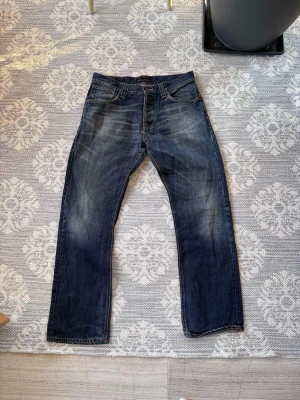Mörkblå raka jeans med slitningar - Snygga mörkblå jeans med raka ben och coola slitningar framtill. Klassisk femficksmodell med orangea sömmar och knappgylf. Perfekta för en avslappnad och trendig stil.