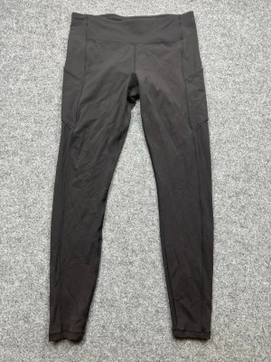 Svarta leggings från Lululemon - Snygga svarta leggings från Lululemon med hög midja och smickrande passform. Tillverkade i stretchigt och mjukt material, perfekta för träning eller chill. Praktiska sidfickor och diskret logga på benet.