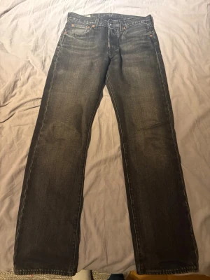 Levi's 501 svarta raka jeans - Klassiska svarta Levi's 501 jeans med rak passform och fem fickor. Jeansen har en snygg tvättad look och ikonisk läderpatch bak i midjan. Använda fåtal gånger i super skick
