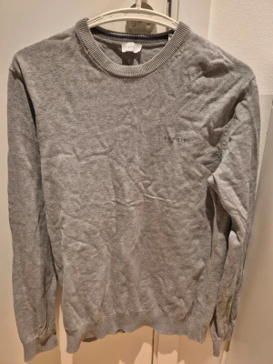Grå stickad tröja Esprit S - Snygg grå stickad tröja från Esprit med rund halsringning och diskret broderad logga på bröstet. Tröjan har långa ärmar och ribbade muddar vid ärmslut och nederkant.