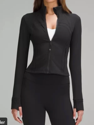 Svart Define Jacket från Lululemon - Snygg svart träningsjacka från Lululemon med figurnära passform, hel dragkedja och tumhål vid ärmsluten. Tillverkad i stretchigt och mjukt funktionsmaterial som andas. Endast använd fåtal gånger! Är i storlek S (4)