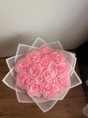 Bukett med rosa konstgjorda rosor - Säljer en bukett med ljusrosa konstgjorda rosor, arrangerade i ett dekorativt vitt omslag. Rosorna har en realistisk form och är tillverkade i ett mjukt material som liknar plast eller skum. Perfekt som dekoration eller present.