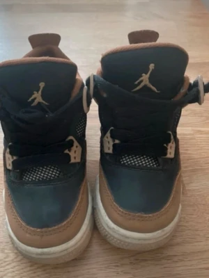 Jordan sneakers svart/brun meshdetaljer - Snygga sneakers från Jordan i svart och brunt med vita sulor. Skorna har meshdetaljer på sidorna och tungan, samt klassisk Jumpman-logga i guld på plösen. Ovandelen är i en mix av textil och syntetmaterial med coola plastdetaljer vid snörningen.