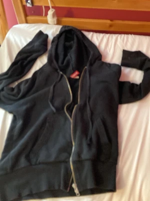 Svart hoodie med huva - En klassisk svart hoodie med dragkedja och huva. Hoodien har snören i huvan och ribbade muddar vid ärmslut och nederkant. Perfekt för en avslappnad och chill stil. Tillverkad i Turkiet. Den är i storlek 36. Har använt den några få gånger 🧥