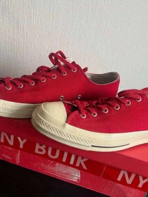 Converse all star Chuck Taylor II - Klassiska röda Converse sneakers i canvas med vita gummisulor och tåhätta. Skorna har silverfärgade öljetter och röda skosnören. Den låga modellen gör dem perfekta till jeans eller shorts. Tidlös design som alltid är rätt.