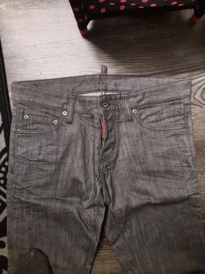 Grå raka jeans från Dsq2 - Säljer ett par grå jeans från Dsq2 med klassisk femficksmodell och raka ben. Jeansen har en diskret tvätt och silverfärgade nitar. Materialet är denim i bomull och passformen är rak. Perfekta för en clean och stilren look. Mätter om de behövs storlek 46 i dsq2 storlek  👍 Helg rea nu 👍