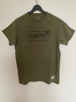  Levi's t-shirt  - Säljer en olivgrön t-shirt från Levi's med stor svart logga på bröstet och en liten patch nertill. Klassisk passform och rund halsringning. Tillverkad i 100% bomull för skön känsla och andningsförmåga. Perfekt till jeans eller shorts. Bröstvidd:47,5  Längd:65