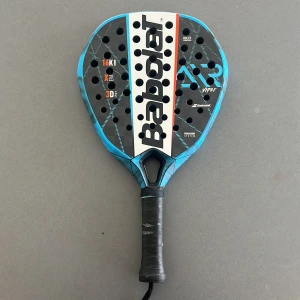 Babolat Viper padelracket blå - Säljer ett Babolat Viper padelracket i blått och svart med vita och orange detaljer. Racketen har droppform, perforerad träffyta och svart grepp med handledsrem. Perfekt för dig som vill ta ditt padelspel till nästa nivå. Använd väldigt varsamt och inga sprickor eller spelpåverkande defekter. 