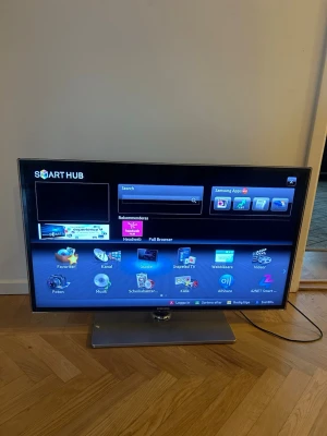 Samsung TV med HDMI och USB - Samsung TV med platt skärm och silverfärgad fot. Utrustad med flera HDMI-portar, USB-ingångar och digital ljudutgång. Smart Hub för appar och webbläsare. Perfekt för streaming och anslutning av olika enheter. 40tum. 