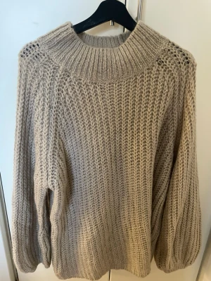 Beige chunky stickad tröja - Säljer en beige chunky stickad tröja med bred ribbad polokrage och grovstickat mönster. Tröjan har långa ärmar och en avslappnad passform, perfekt för kyliga dagar. I materialet ull/ullmix