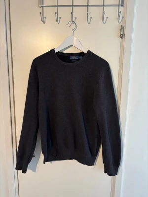 Polo Ralph Lauren tröja   - Snygg mörkgrå tröja från Polo Ralph Lauren i mjuk pima bomull. Klassisk rund halsringning och ribbade muddar vid ärmslut och nederkant. Perfekt basplagg för en clean och stilren look.