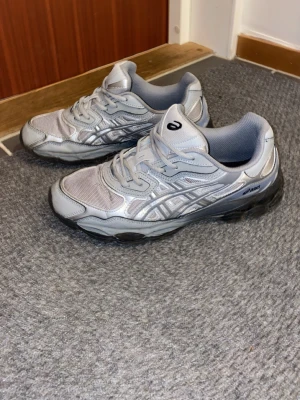 Asics Gel-NYC sneakers silvergrå - Säljer ett par Asics Gel-NYC sneakers i silvergrå färg med mesh och syntetpaneler. Skorna har snörning, rund tå och en chunky sula som ger retrovibbar. Perfekta för dig som gillar sportig stil och streetwear. På lappen så står det att skorna är 44.