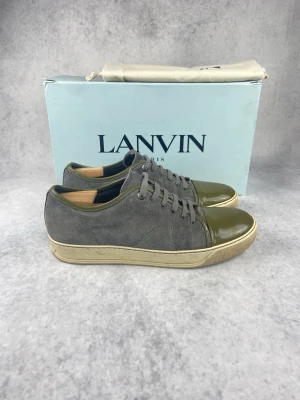 Gråa och olivgröna Lanvin sneakers - Snygga sneakers från Lanvin i grå mocka med olivgrön lackad tå och häl. Skorna har beige sula och tonade skosnören. Perfekt för dig som gillar stilrena men unika detaljer. Kommer med originalkartong.