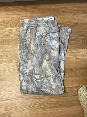 Hollister camomönstrade bootcut mjukisbyxor  - Säljer ett par grå camomönstrade mjukisbyxor från Hollister. Byxorna har dragsko i midjan och är tillverkade i mjukt polyestermaterial. Perfekta för en avslappnad och chill stil.