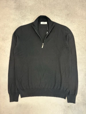 Svart halvzip-tröja Gran Sasso - Klassisk svart stickad tröja från Gran Sasso med halv dragkedja och hög krage. Tröjan har ribbade muddar vid ärmslut och nederkant. Perfekt för en stilren och enkel look. Tillverkad i mjukt material för extra komfort. Vi har tröjan i både storlek M och L.
