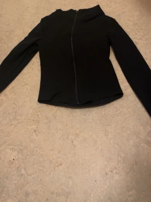 Svart ziptröja tränings material  - Snygg svart ziptröja med hög krage och långa ärmar. Tröjan har en smal passform och dragkedja framtill. Perfekt att slänga på sig över en t-shirt för en clean look. Tränings material från Ginatricot 