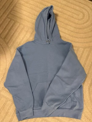 Blå hoodie från Monki - Säljer en ljusblå hoodie från Monki i storlek S. Hoodien har en klassisk känguruficka framtillPerfekt för en chill och avslappnad stil. Materialet är mjukt och skönt mot huden.