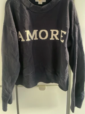 Mörkblå stickad tröja med AMORE - Snygg mörkblå stickad tröja från Gina Tricot med vit text 'AMORE' framtill. Tröjan har en klassisk rund hals och långa ärmar.