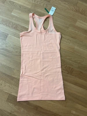 Ljusrosa ärmlös linnetopp - Ljusrosa linnetopp med brottarrygg och figurnära passform. Toppen är ärmlös och tillverkad i mjuk bomull med stretch. Enkel och stilren utan tryck eller logga, perfekt för sommaren.