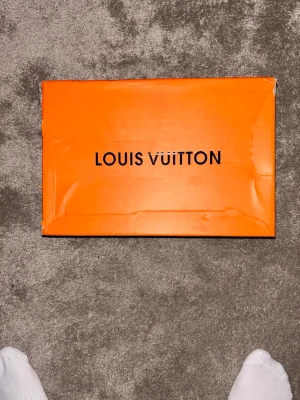 Louis Vuitton trainers - Säljer en ikonisk orange skokartong från Louis Vuitton med svart logotyp på locket. Perfekt för dig som vill ha en snygg förvaring eller vill komplettera din samling av designeraccessoarer. Kartong lite sliten samt skorna men inget ögat märker.