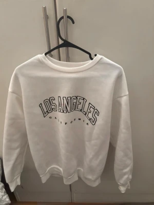 Vit sweatshirt med Los Angeles-tryck - Vit sweatshirt med svart text 'Los Angeles California' på bröstet. Tröjan har rund halsringning och långa ärmar med ribbade muddar. Perfekt för en avslappnad och trendig look. För mer bilder/justering av pris skriv gärna❤️🤗