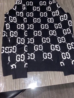 Äkta Gucci sweatshirt - Svart stickad tröja med vitt GG-mönster över hela plagget. Tröjan har ribbade muddar vid ärmslut och nederkant. Oversized känsla och trendig look, perfekt för dig som gillar streetstyle och loggor.