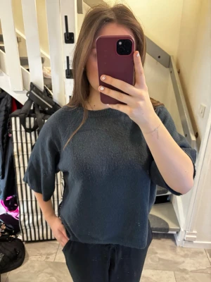 Mörkblå kortärmad stickad tröja - En enkel och stilren mörkblå stickad tröja med korta ärmar och rund halsringning. Tröjan har en rak och något boxig passform, perfekt för en avslappnad look. Materialet ser ut att vara mjukt och bekvämt.