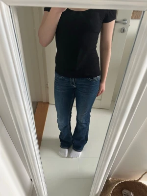 Mörkblå bootcut jeans med kontrastsömmar - Snygga mörkblå bootcut jeans med vita kontrastsömmar och klassiska fem fickor. Jeansen har låg midja och lätt utsvängda ben. Perfekta för en avslappnad och trendig look.