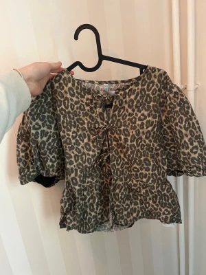 Leopardmönstrad blus med snörning - Trendig blus med leopardmönster och puffiga korta ärmar. Toppen har snygg snörning framtill och en lätt croppad passform. Knappt använd 