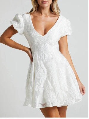 Vit kort klänning med puffärm - Superfin vit kort klänning med v-ringning, puffärmar och subtilt blommönster i tyget. Klänningen har en öppen rygg och är tillverkad i ett tyg med struktur som ger en lyxig känsla. Perfekt för sommarens alla tillfällen. PRISLAPP KVAR!!! Från showpo