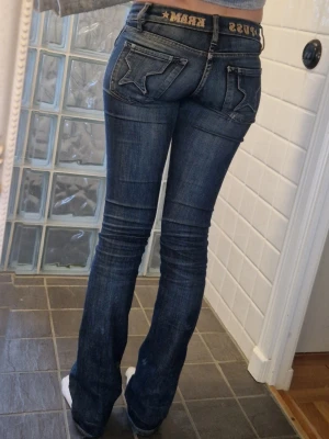 Puss & kram jeans ⭐️ - Säljer ett par blå jeans från Puss Kram med coola stjärndetaljer på bakfickorna och broderad text i midjan. Jeansen har en klassisk femficksmodell och lätt utsvängda ben. Perfekta för dig som vill ha en unik och trendig look. Tecken på användning finns – lite slitna vid innerbenet (se bild 5), men inget som syns när de är på eller som man tänker på! ☺️⭐️ Strl: 28 Midjemått: 37 cm Innerbenslängd: 83 cm