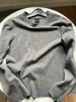 Grå stickad tröja från WeekdayGina Tricot  - Gina Tricot Säljer en enkel och stilren grå stickad tröja från Weekday. Tröjan har rund halsringning, långa ärmar och är gjord i mjukt stickat material. Perfekt basplagg för lager på lager och funkar året runt.