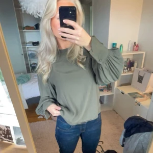 Olivgrön blus med puffärmar - Skitsnygg trendig olivgrön blus med långa puffärmar och breda manschetter. Blusen har en avslappnad passform och är tillverkad i ett mjukt, lätt material som ger ett snyggt fall. Perfekt att styla med jeans eller kjol för en cool look. Storlek M men passar mer S och XS, väldigt bra skick från H&M 