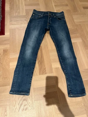 Jack N jones slim fit - Snygga mörkblå jeans med raka ben och klassisk femficksdesign. Jeansen har diskreta slitningar framtill och kontrastsömmar. Perfekta för en avslappnad och trendig look.